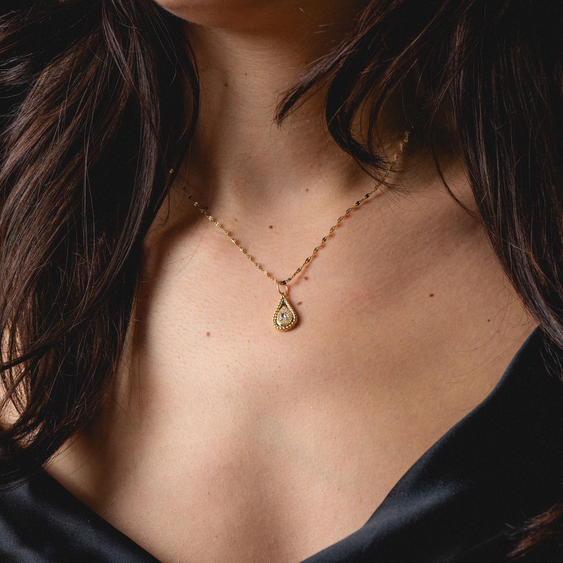 A woman in a black off-shoulder top showcases the Solid Gold 2026 April Capsule Tethered Teardrop White Topaz Charm, its elegant teardrop pendant centered on her collarbone for a timeless, sophisticated look.