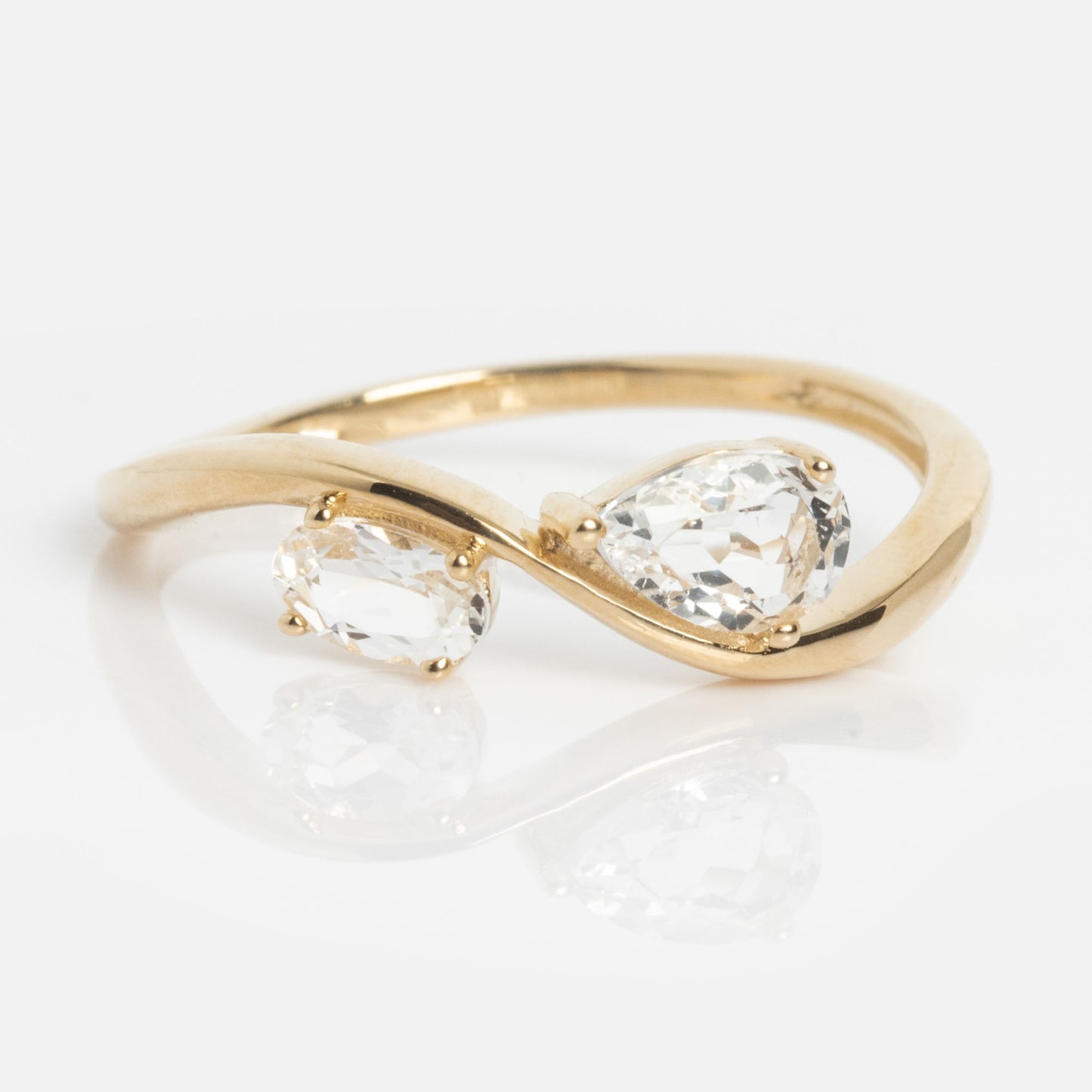 The Solid Gold 2026 April Capsule Floating Duo White Topaz Ring is a limited edition piece with an open, twisting band, showcasing oval and pear-shaped white topaz stones side by side, elegantly displayed on a white background.