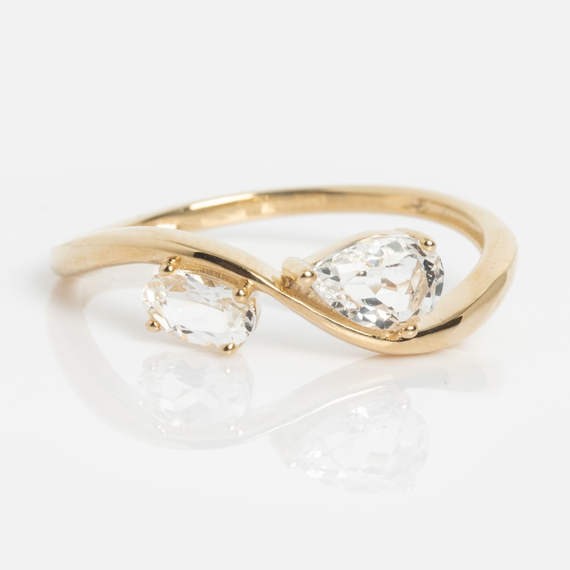The Solid Gold 2026 April Capsule Floating Duo White Topaz Ring is a limited edition piece with an open, twisting band, showcasing oval and pear-shaped white topaz stones side by side, elegantly displayed on a white background.