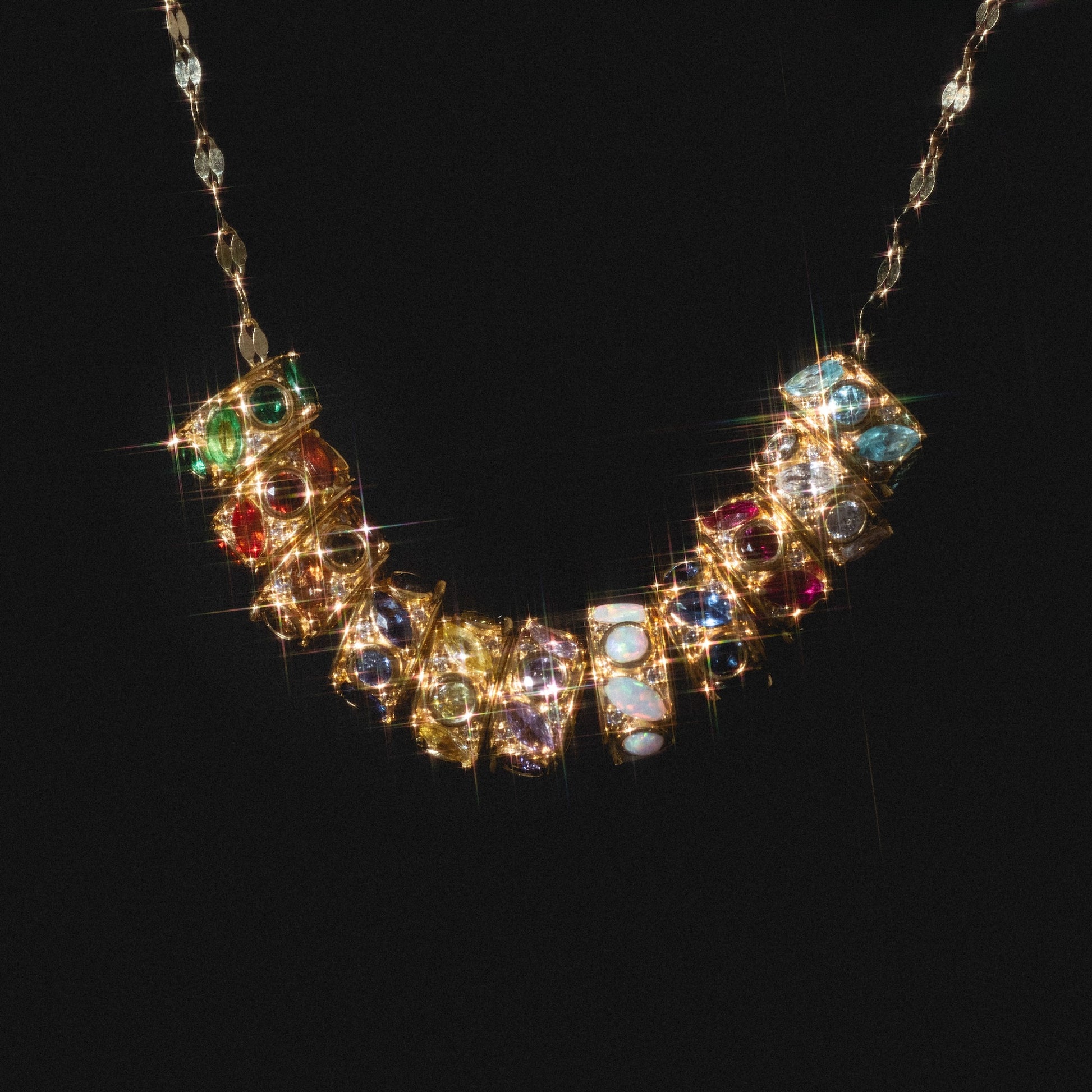 The Shades of You Birthstone Spacer Charm features vibrant, multicolored gemstones set in ornate square designs, each sparkling against a black background.