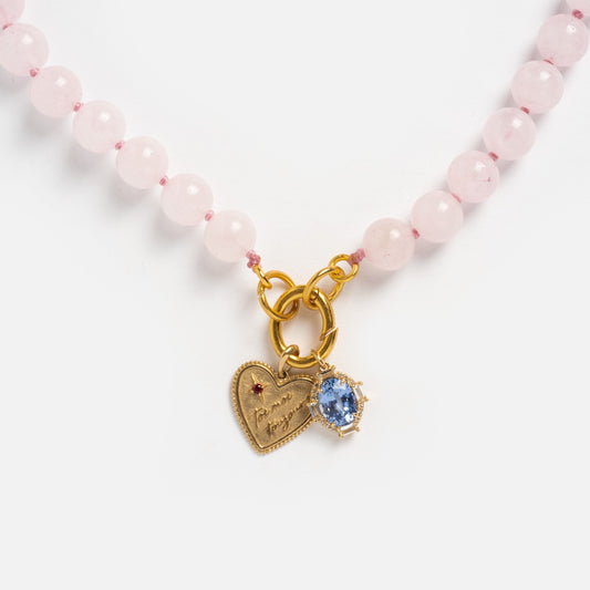 The Beaded Gemstone Charm Holder Necklace features pink beads and two gold charms—one heart-shaped with an engraved message and red gem, the other oval with a blue gem—ideal for fans of gemstone statement necklaces.