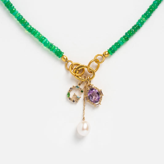 The Sale! Beaded Gemstone Charm Holder Necklace features green beads, gold chain links, and three pendants: a green stone letter C, a purple gemstone charm in gold, and a dangling white pearl—an eye-catching beaded necklace.