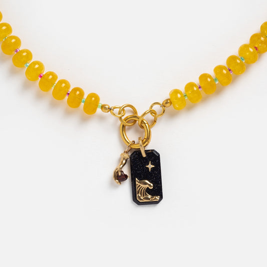 The Sale! Beaded Gemstone Charm Holder Necklace showcases yellow beads, a gold ring clasp, a black rectangular pendant with a gold wave and star design, and a small gold charm with a dark red stone—ideal for gemstone necklace lovers.