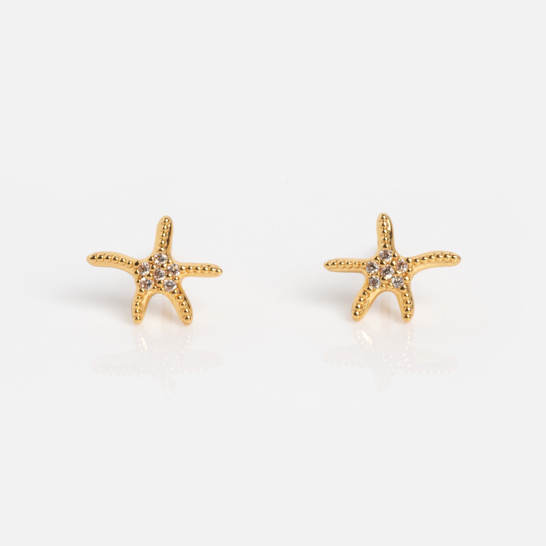The Shimmering Starfish Studs are gold, starfish-shaped earrings featuring small clear stones, shown on a plain white background.