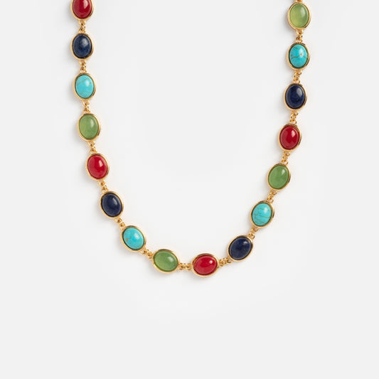 The Bari Choker Necklace is a gold chain with oval gemstones in red, green, blue, and turquoise bezel-set in gold, shown on a plain white background.