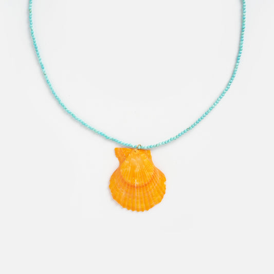 The Byron Necklace is a light blue beaded necklace with a bright orange scallop shell pendant, shown on a plain white background.