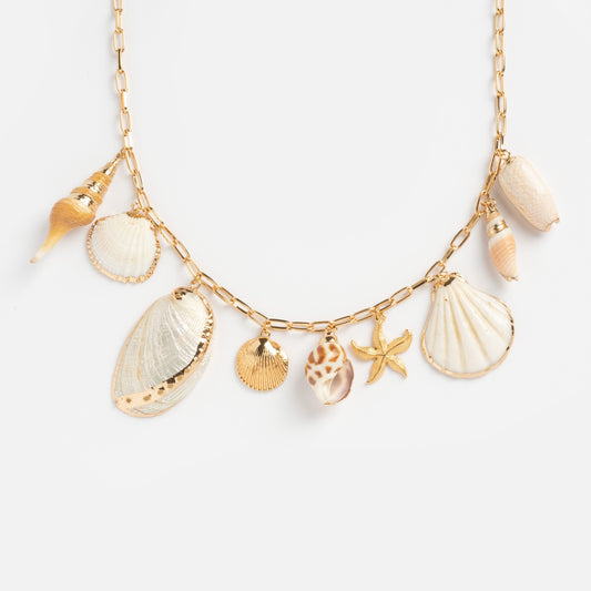 The Private Island Shell Necklace features gold-accented seashell and starfish charms on a gold chain, displayed against a light, neutral background.