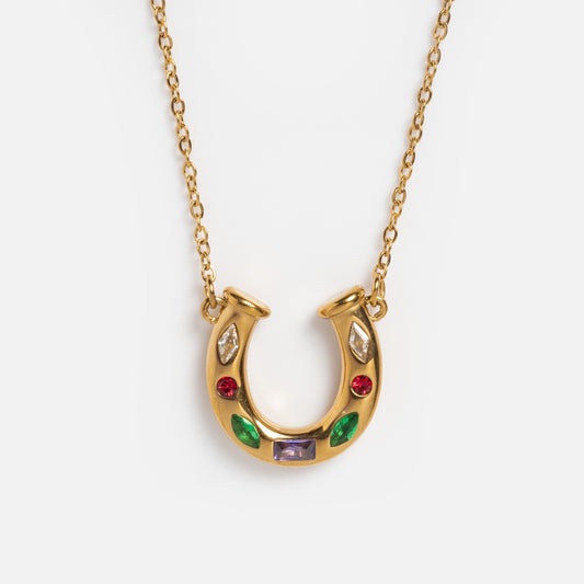 The Horseshoe Gem Necklace is a gold pendant necklace with a horseshoe-shaped charm embellished with vibrant red, green, purple, and clear gemstones for an elegant look.