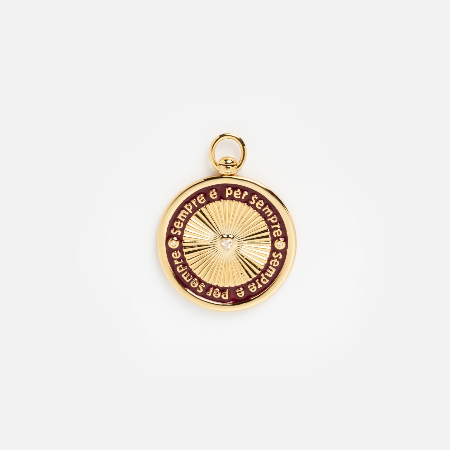Charms by Mod + Jo: A round gold pendant featuring a central sunburst, inspired by classic gold-plated charms, with "è per sempre" engraved repeatedly in a ring on a maroon-edged background.