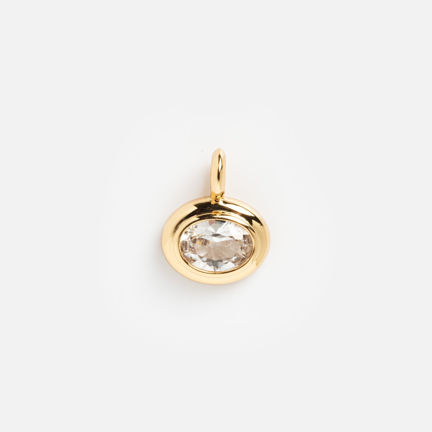 The Charms by Mod + Jo gold pendant features an oval clear gemstone at the center, symbolizing good luck. Photographed against a white background, this elegant piece adds a touch of charm to any look.