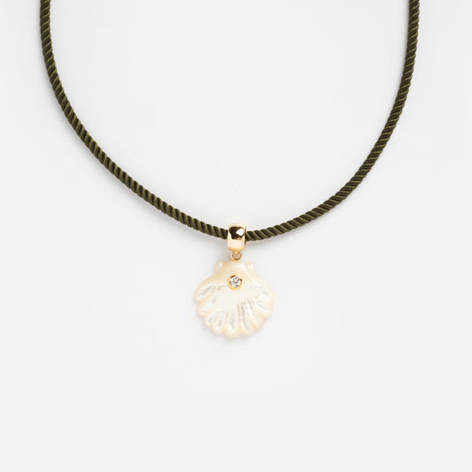 The Coquille Silk Cord Necklace features a dark green silk cord with a gold bail holding a shell-shaped pendant adorned with a small gem, shown on a plain white background.