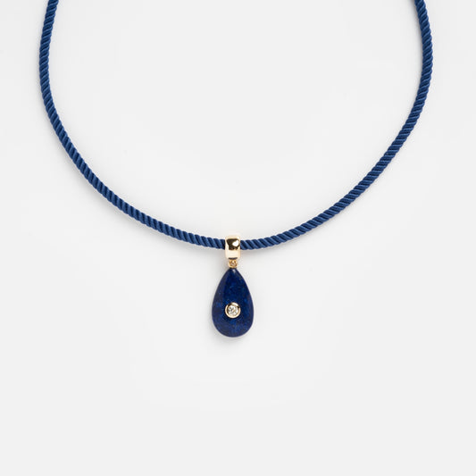 The Bardot Silk Cord Necklace features a blue silk cord, a gold bail, and a teardrop-shaped blue pendant with a central round gem, displayed on a plain white background.