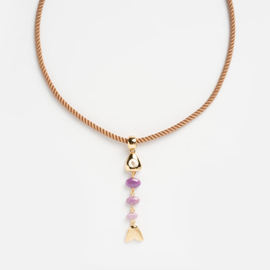 The La Pez Silk Cord Necklace features a tan silk cord with a gold pendant, showcasing a pearl, three purple beads, and a tail-shaped gold charm arranged vertically for an ocean-inspired look.