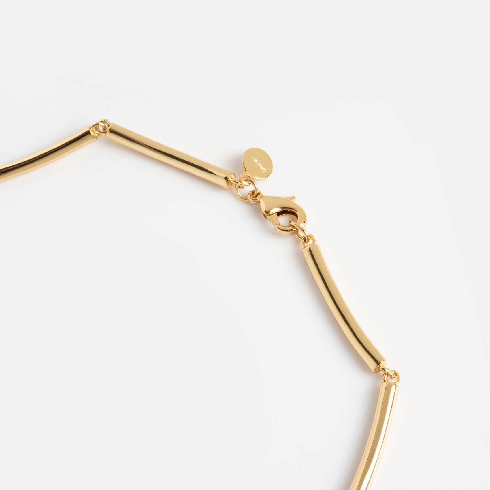 Close-up of the Hayes Collar Necklace—a gold piece with elongated tubular links, lobster clasp, and small round tag near the clasp—displayed on a plain white background.