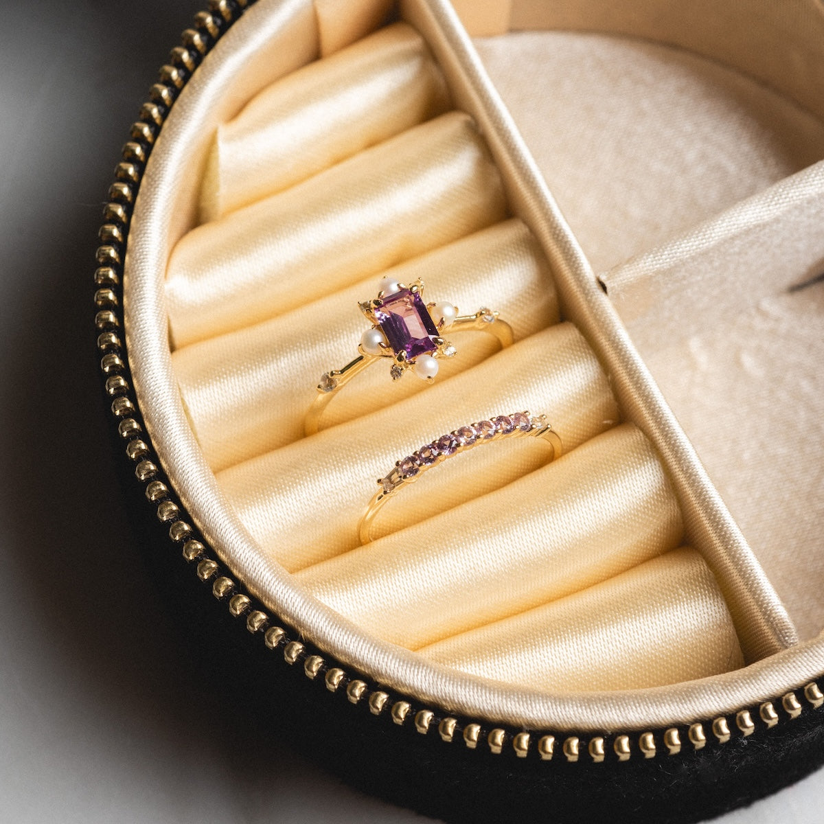 The Solid Gold 2025 June Capsule Alexandrite and Pearl Ring Set includes a gold alexandrite ring with pearls, a stacking ring with pink stones, and comes in a jewelry box with a padded cream interior and gold zipper. Free gift included.