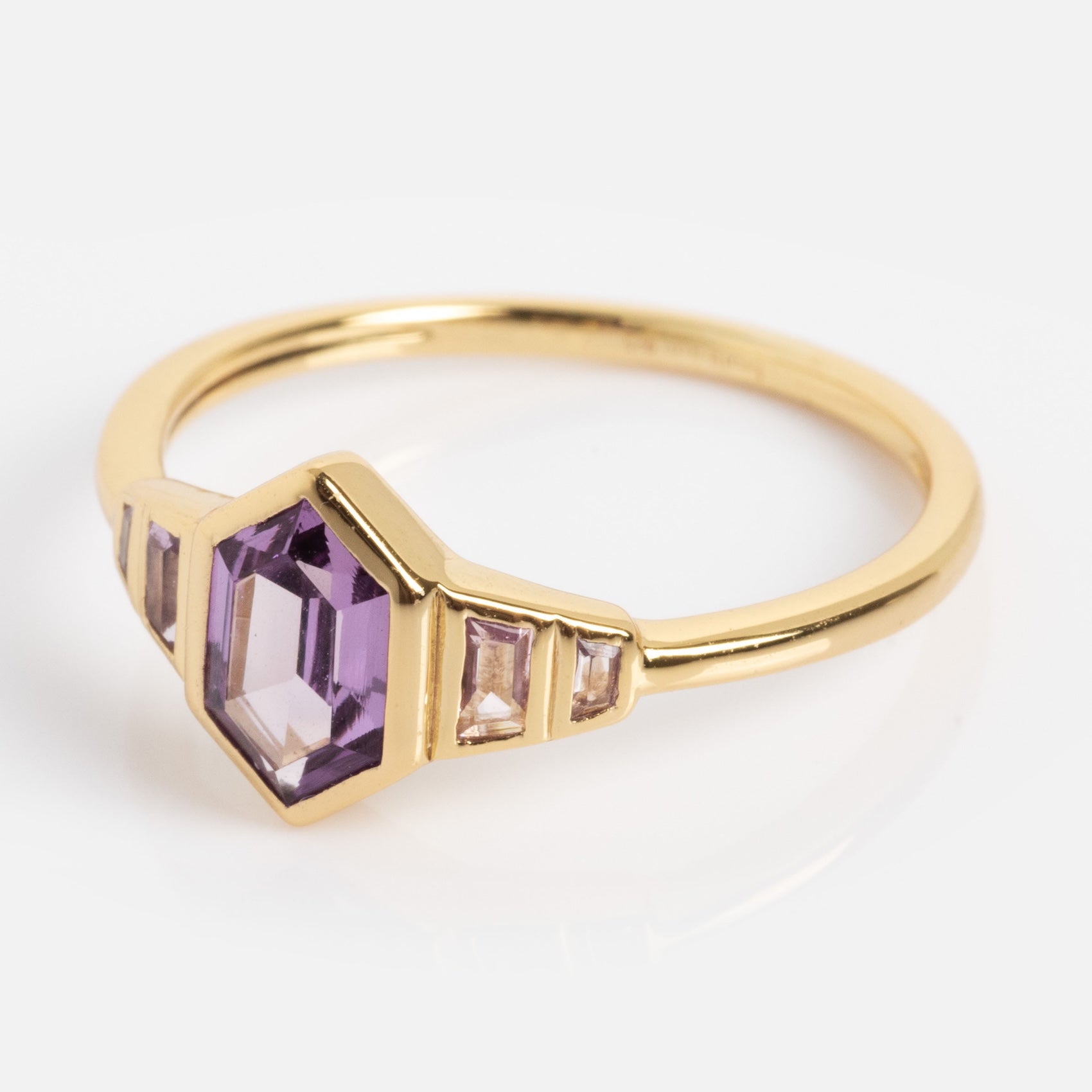 The 2026 June Capsule Art Deco Alexandrite Ring features a gold band with a hexagonal purple alexandrite center stone and rectangular clear side stones, shown on a white background.