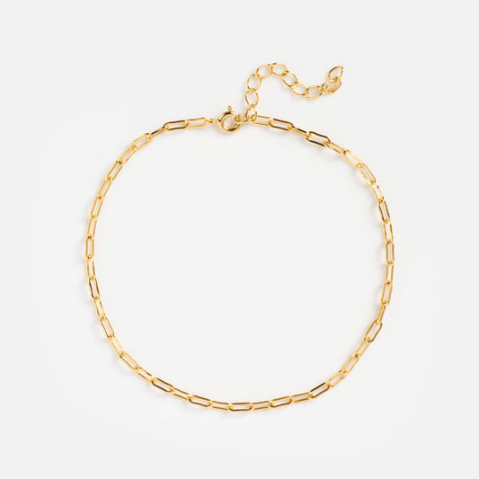 The Paperclip Chain Anklet features elongated oval links and an adjustable clasp, shown in a circular shape on a white background—ideal to wear solo or layered with your favorite anklets for a chic gold look.