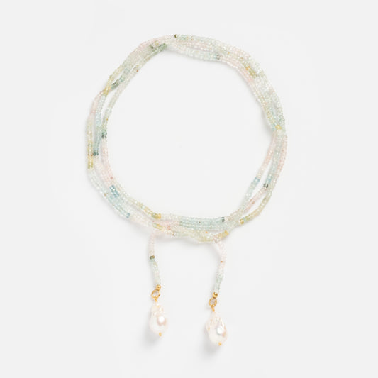 The Gemstone Tie Necklace is a delicate, multi-strand adjustable lariat featuring pastel gemstone beads and two dangling white pearls with gold accents at the ends, artfully arranged in a loose coil on a white background.