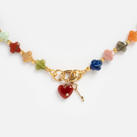The Beaded Gemstone Charm Holder Necklace showcases multi-colored flower beads, gold links, a jeweled red heart pendant, and a gold key charm—all displayed on a white background.