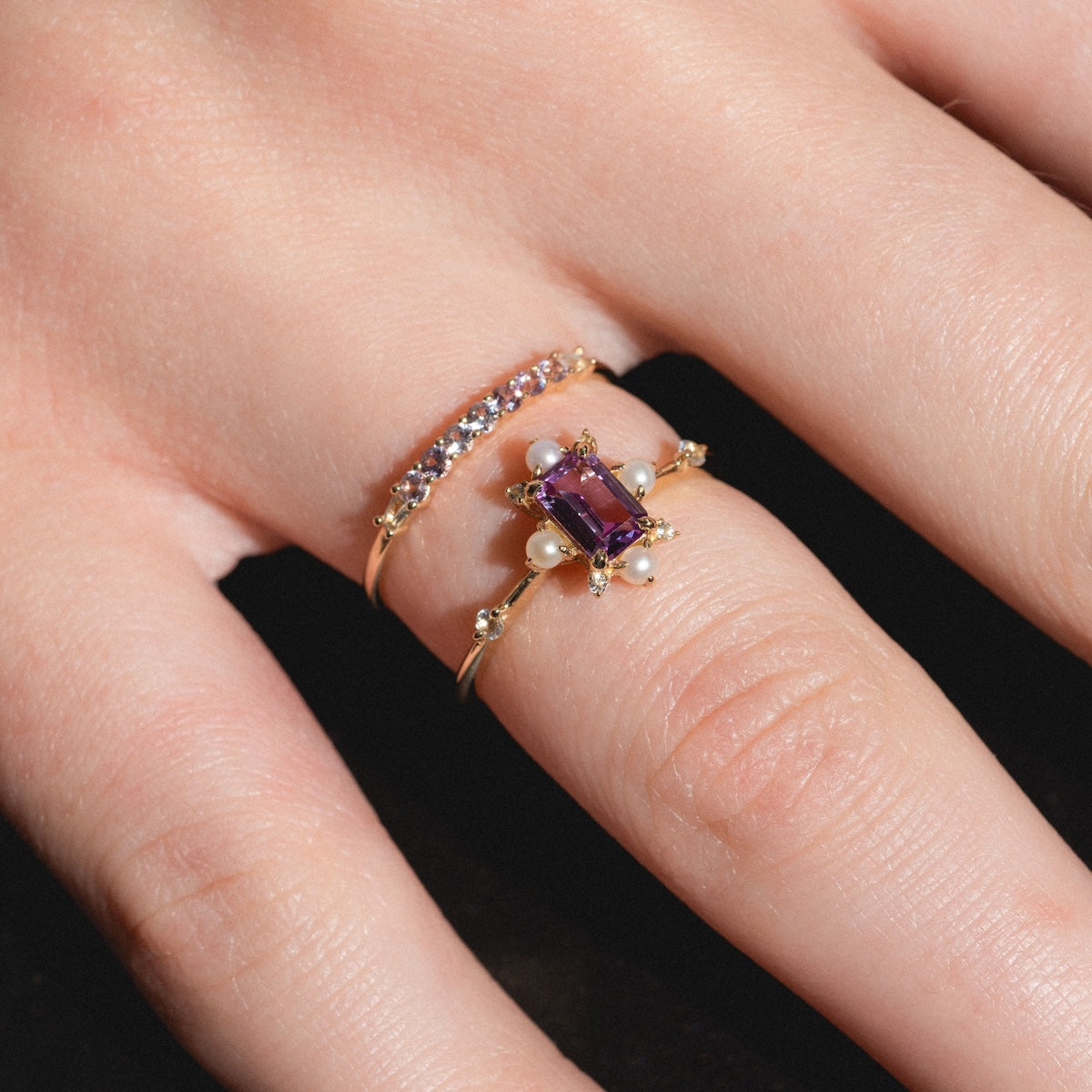 A hand wears the Solid Gold 2025 June Capsule Alexandrite and Pearl Ring Set—a rectangular purple alexandrite with pearl accents, plus a band of clear stones—perfect for June birthstone fans. Includes a free gift.