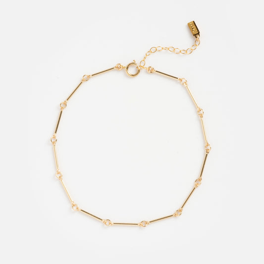 The Lee Anklet is a delicate gold chain with small bar and knot links, featuring an adjustable extension and round clasp—perfect as understated vacation jewelry—shown on a white background.