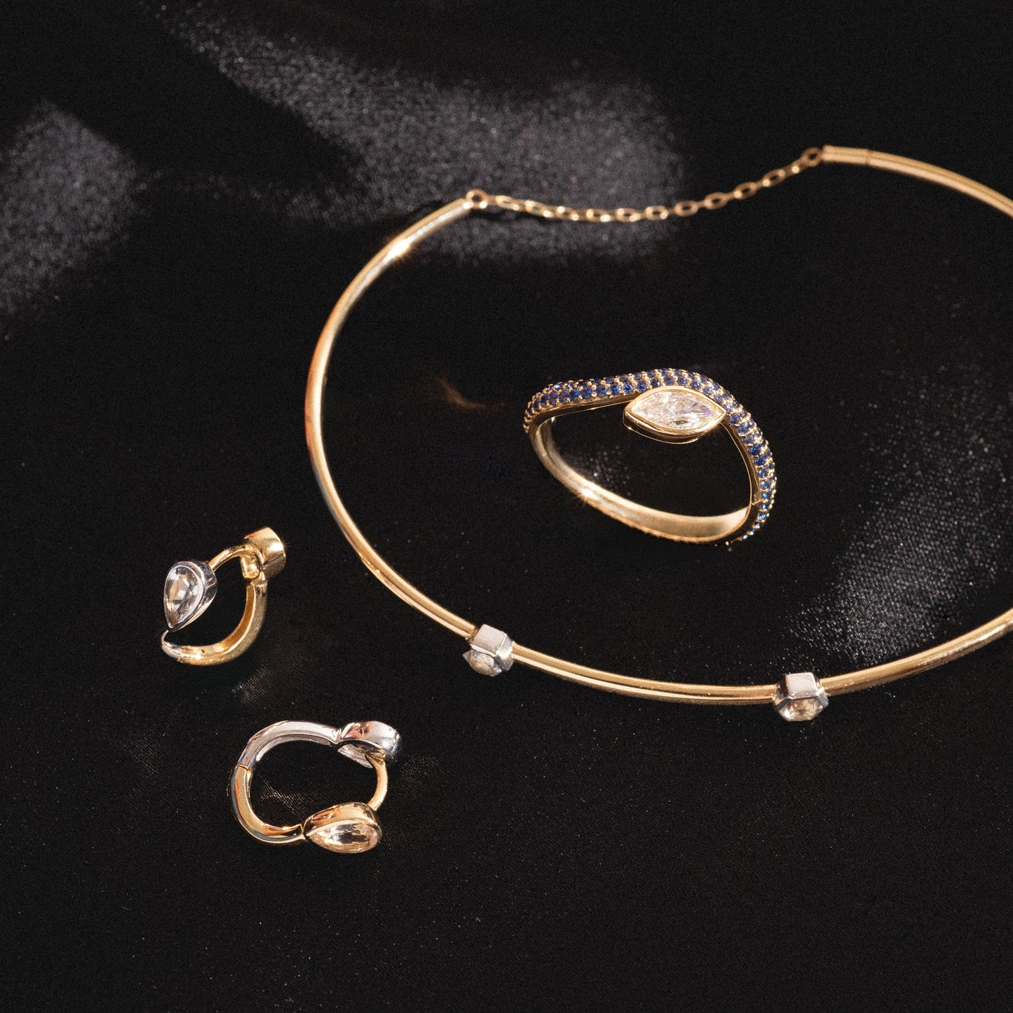 The Solid Gold Mixed Metal Duo Huggies, adorned with sparkling clear gemstones, are elegantly displayed on black satin fabric.