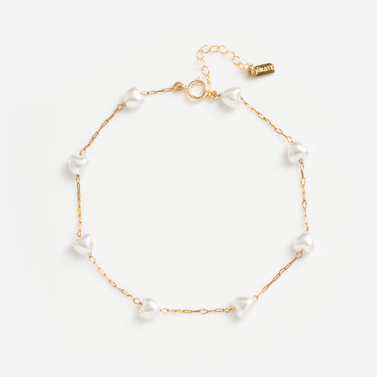 The Hearts Anklet is a delicate 18k gold piece with evenly spaced small simulated pearls, an adjustable clasp, and a petite gold tag.