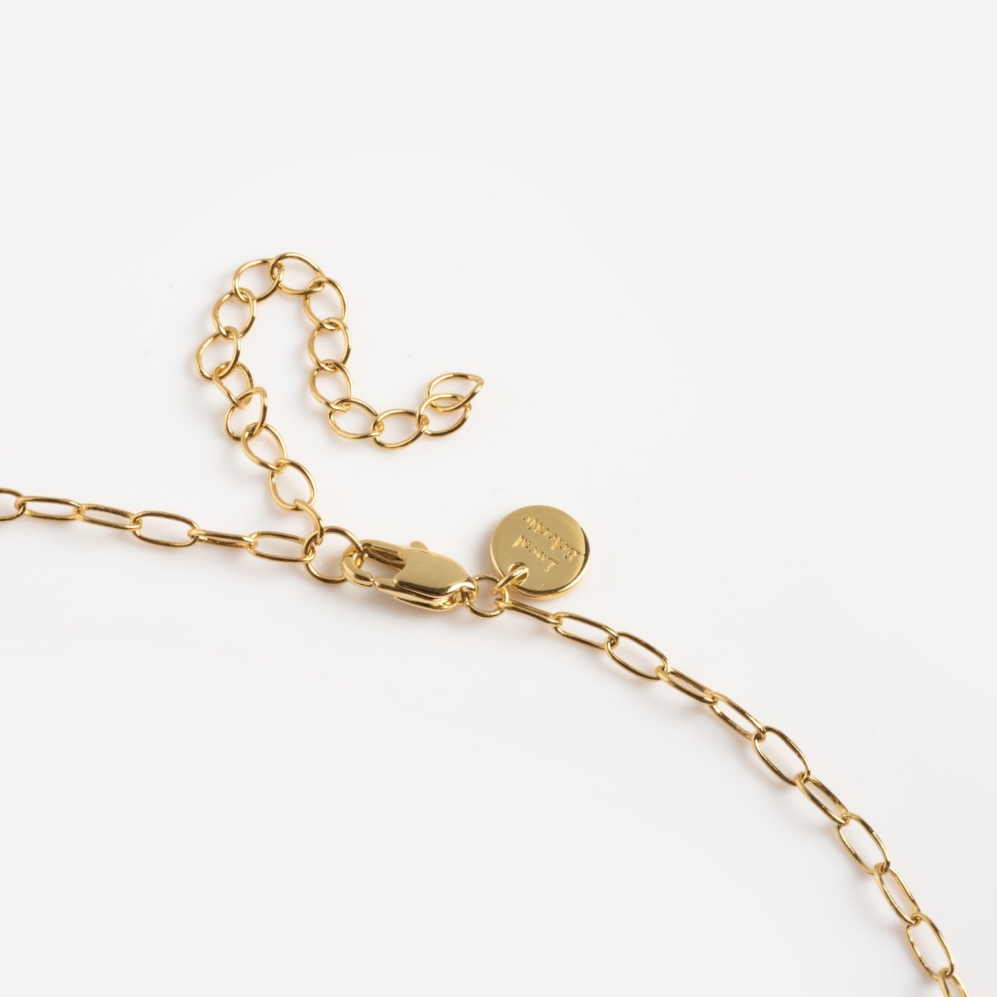 Close-up of the Kiss More Girls Necklace featuring gold elongated oval links, a lobster clasp, adjustable extension, and a small round tag, shown on a white background.