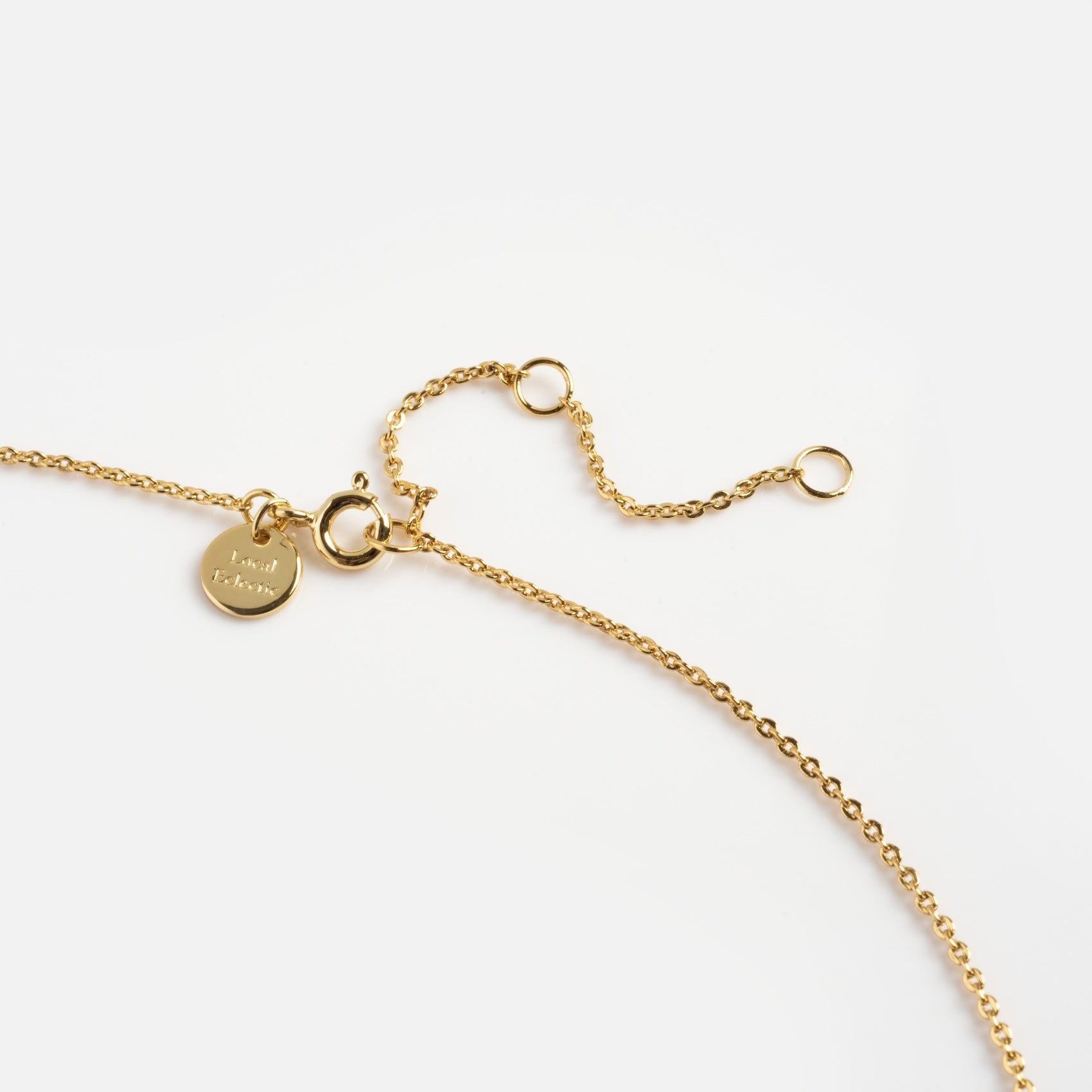 The Kiss More Boys Necklace features a delicate gold chain with an adjustable clasp and a small engraved round charm, showcased against a plain white background.