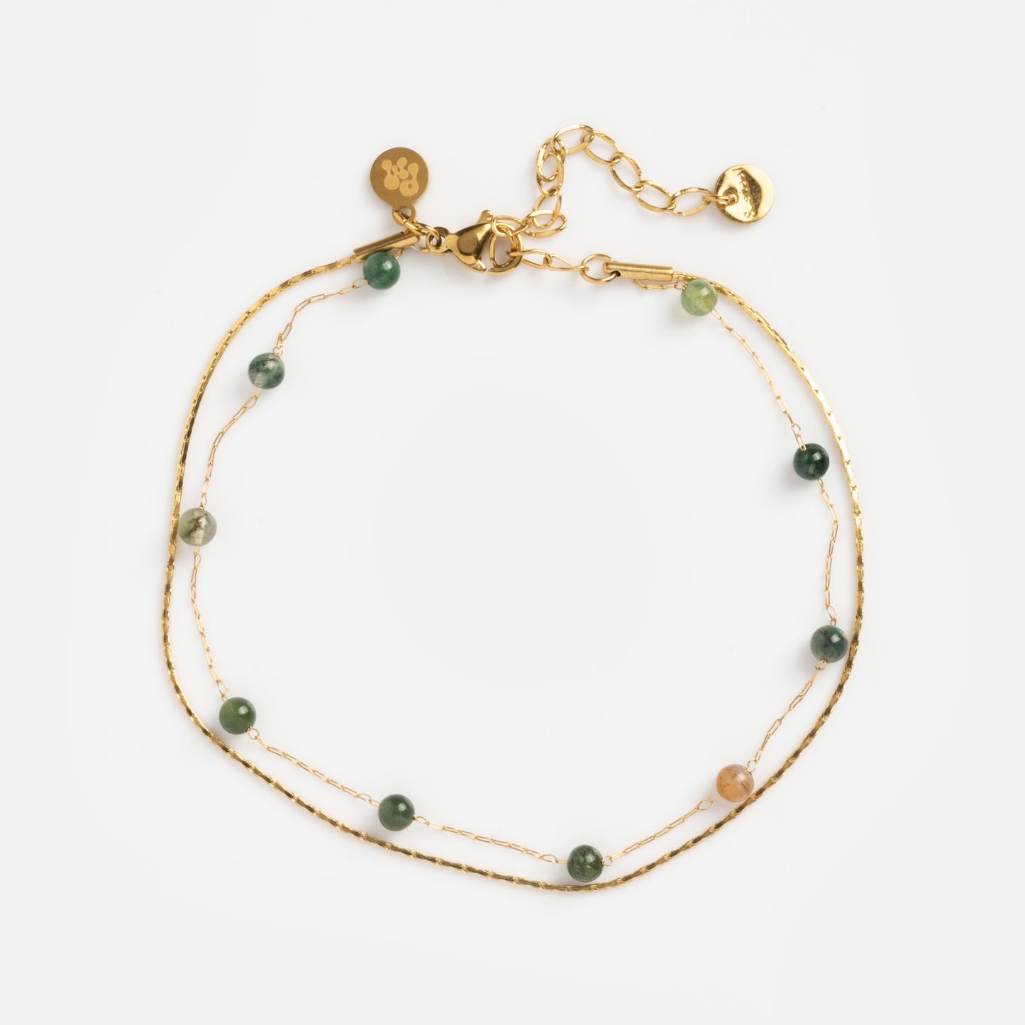 The Alexis Anklet features two delicate gold chains with small green and beige beads, an adjustable clasp, and gold charms, all shown against a white background.