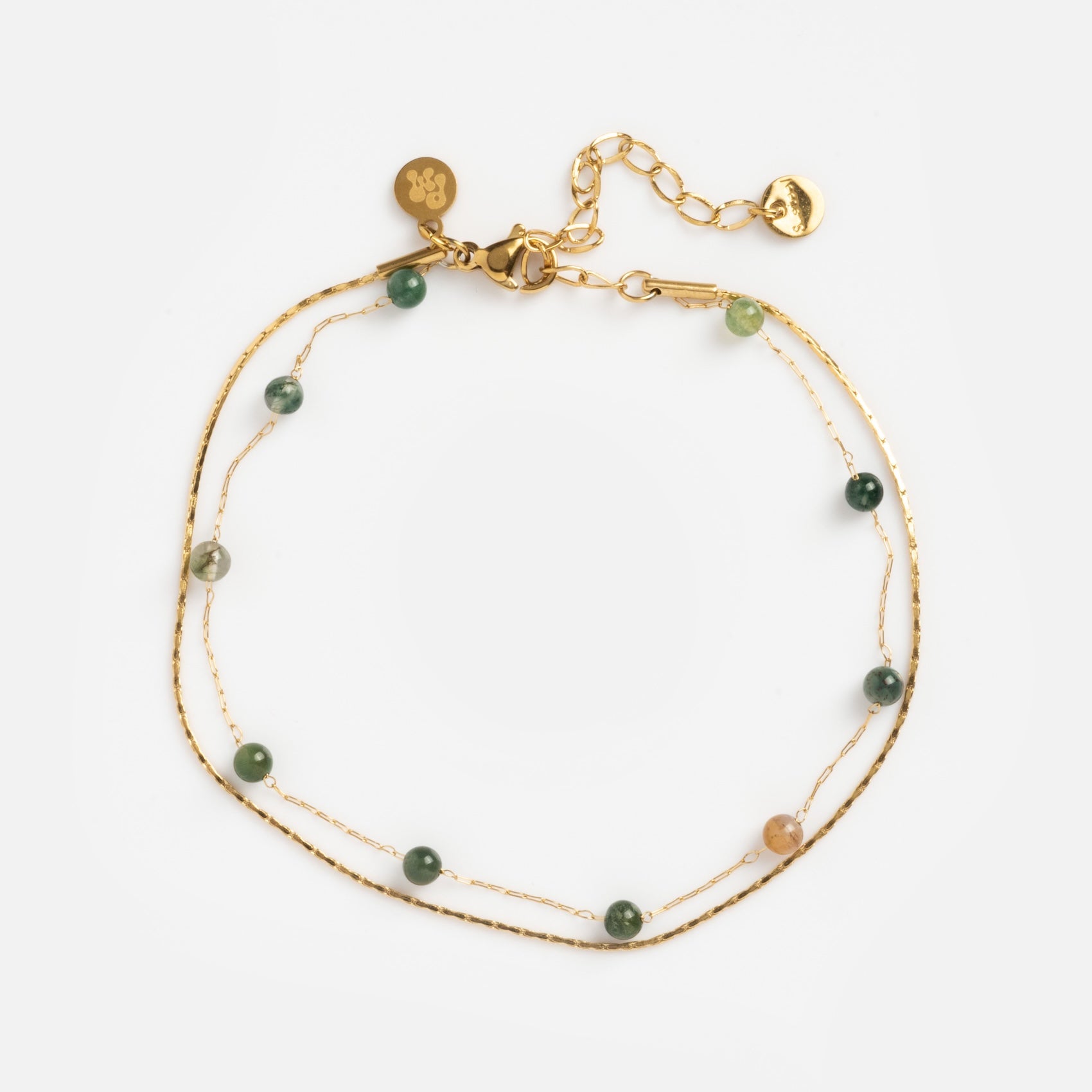 The Alexis Anklet features two delicate gold chains with small green and beige beads, an adjustable clasp, and gold charms, all shown against a white background.