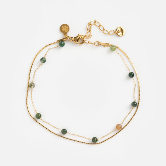 The Alexis Anklet features two delicate gold chains with small green and beige beads, an adjustable clasp, and gold charms, all shown against a white background.