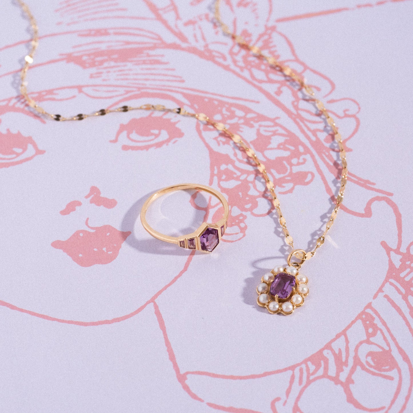 The Solid Gold 2026 June Capsule Art Deco Alexandrite Ring and a matching gold pendant necklace rest on paper with a pink line drawing of a woman's face.