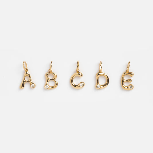 The Solid Gold Diamond Initial Charm Sample features five 9k yellow gold letter charms (A-E), each set with a 2mm lab-created diamond, arranged in a row on a plain white background.