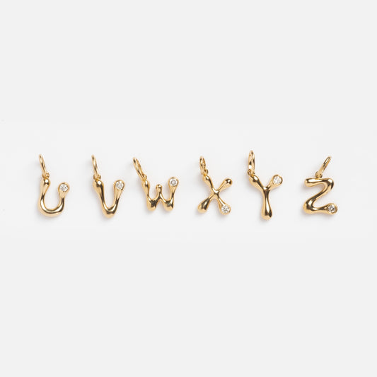 Six 9k solid yellow gold charms shaped as the lowercase letters u, v, w, x, y, and z each feature a 2 mm lab-created diamond. They are displayed in a row on a white background as Solid Gold Diamond Initial Charm Samples.
