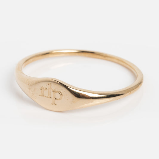 A Solid Gold Engravable Simple Signet Ring, sample engraved with rlp in serif font, features a thin 9k yellow gold band and flat oval face. Shown in size 10 against a plain white background.