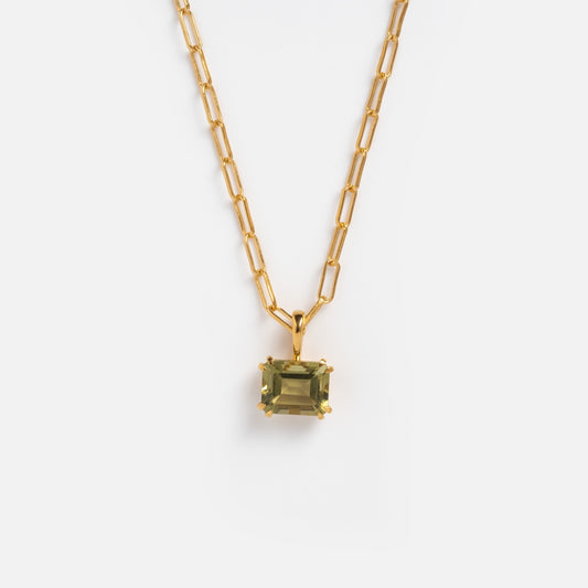 The Plated Birthstone Necklace June Sample is a yellow gold plated chain with elongated links, featuring a rectangular olive-green gemstone pendant in a gold prong setting on a brass base, shown against a white background.