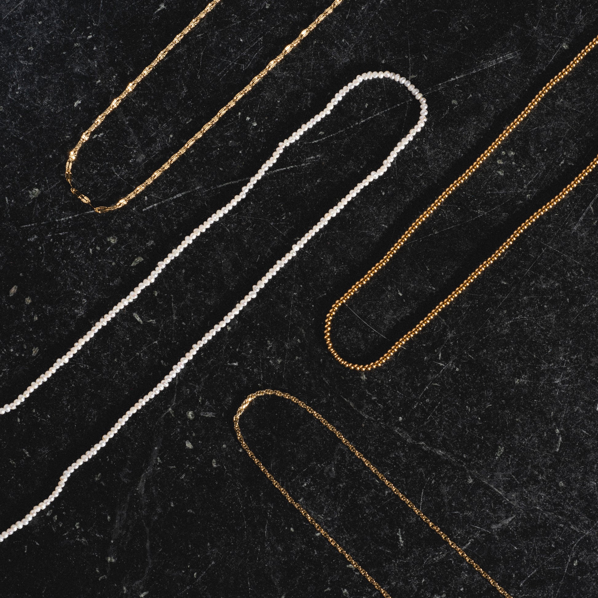 Delicate rope, beaded vermeil, pearl, and sparkle link chains arranged on black marble