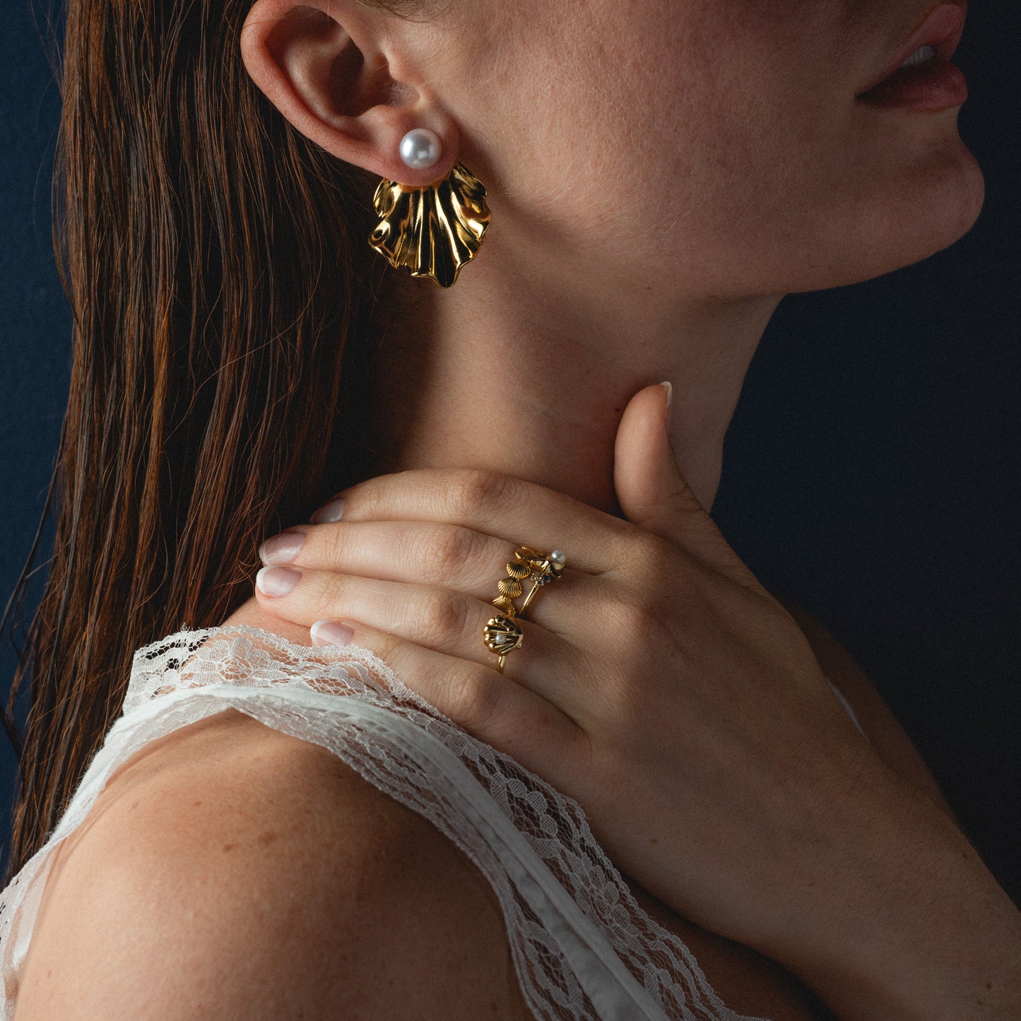 Close-up of a woman wearing gold earrings and a ring against a dark background