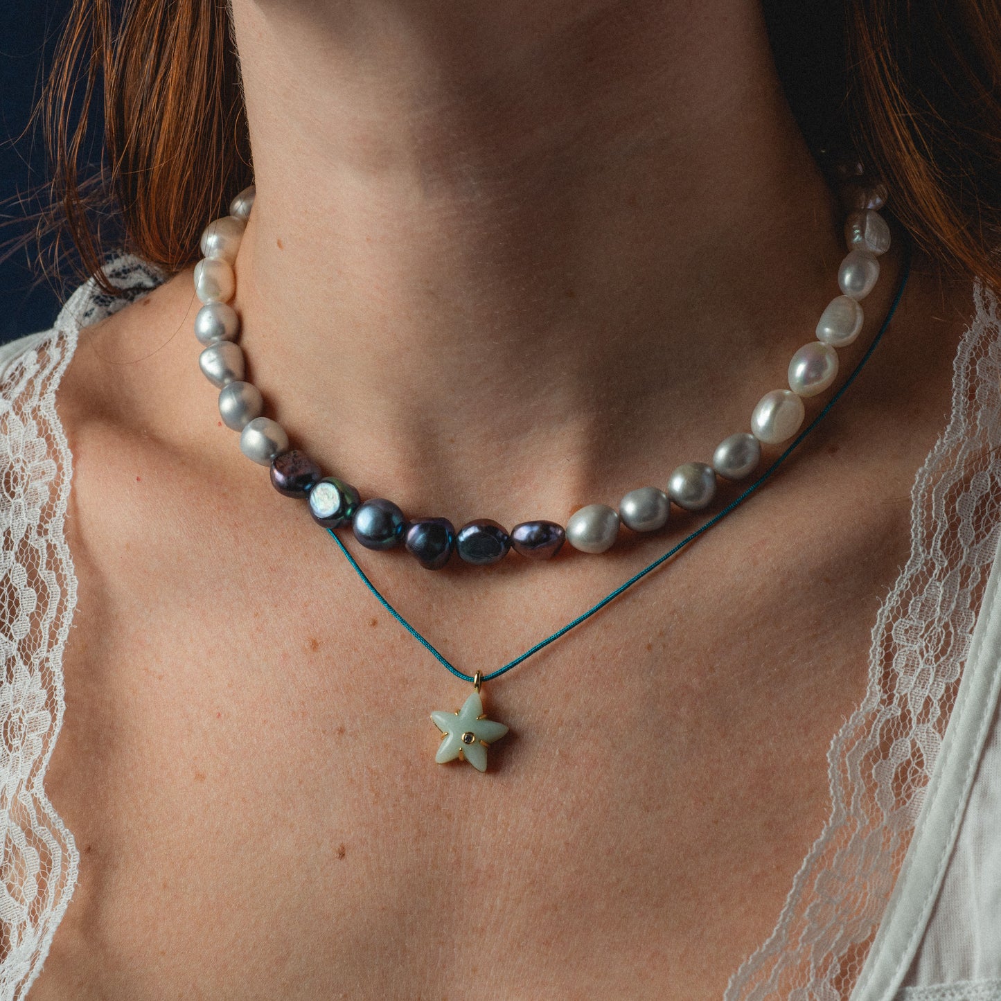 Close-up of a person wearing a pearl and starfish pendant necklace.