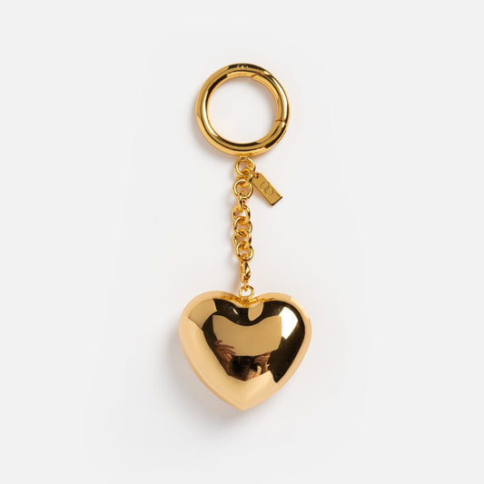 The Heart Bag Charm is a shiny gold keychain with a large metallic heart on a short chain and round keyring. It features a small rectangular tag and makes a perfect statement accessory for girls' crew bags.