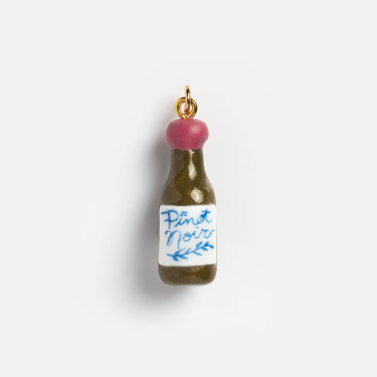 Charms by Warm Clay Co offers a small, hand-crafted wine bottle charm with a pink cap, gold loop, and white Pinot Noir label in blue script with vine design—ideal for creating unique necklace charms.