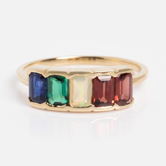 A Customizable Acrostic Baguette Gemstone Ring features garnet, opal, emerald, and sapphire baguettes set side by side on a simple gold band, shown in size 7 against a white background.