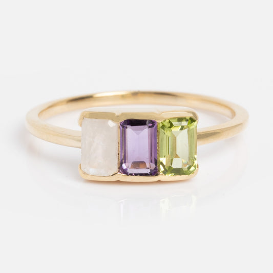 The Customizable Acrostic Baguette Gemstone Ring features peridot, amethyst, and moonstone baguettes set side by side on a thin gold band. Size 6 sample.