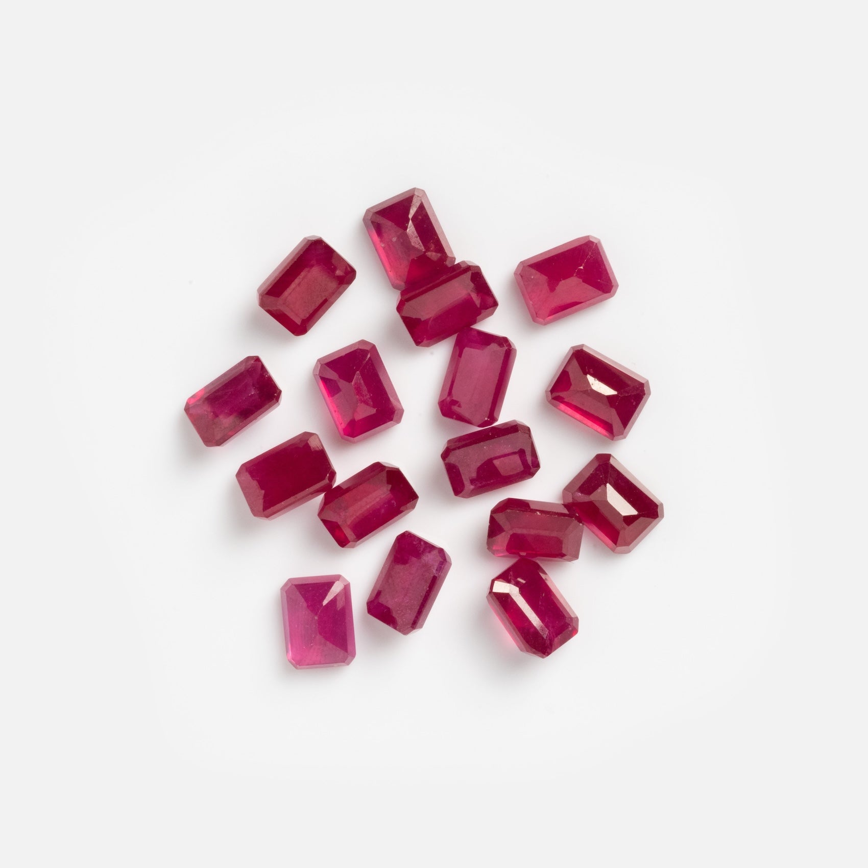 A scattered group of rectangular, faceted 2.7 carat loose ruby samples displayed on a plain white background.