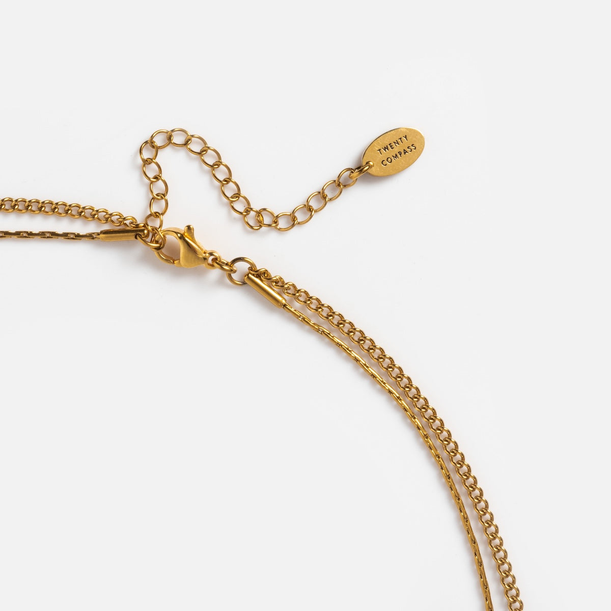 Close-up of the Billie Necklace, a gold layered piece with a lobster clasp, adjustable chain, and a small oval tag reading TINY COMPASS near the clasp, displayed on a white background.
