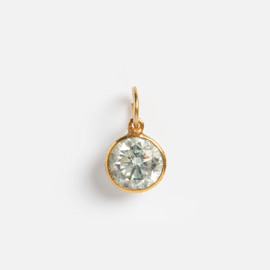 The Gemstone Charms by Anokhi Green features a round, faceted clear moissanite pendant set in a simple 18k gold vermeil bezel with a small gold loop at the top, shown on a plain white background.