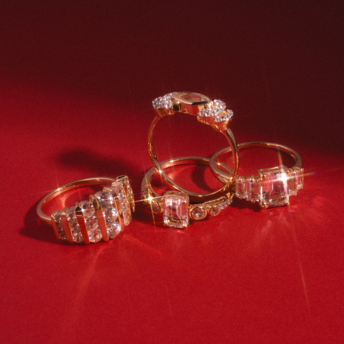 Four solid gold statement rings, including the 14k Regal White Topaz Statement Ring, are displayed on a red surface with bright light accentuating their shine and intricate details.