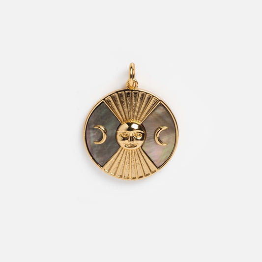 The Charms by Elizabeth Stone pendant is a round 14k gold plated celestial charm with a sun face, downward rays, crescent moons on each side, and a dark mother of pearl inlay. It has a loop at the top for easy attachment to any chain.