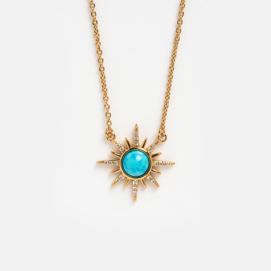 The Gemstone Starburst Necklace features a sun-shaped 14k gold plated pendant with a turquoise center and radiant spikes set with clear stones, showcased on a plain white background.